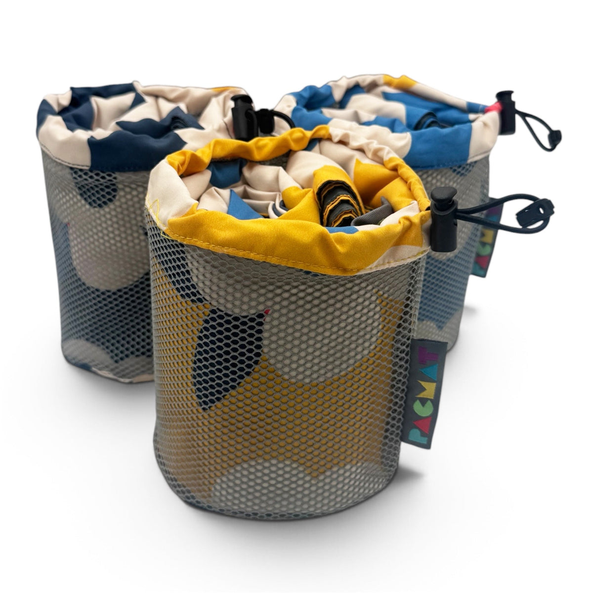 Three cylindrical mesh laundry bags with drawstring tops, shown on a clean white background. The bags feature a gray and navy blue camouflage pattern on the exterior and a yellow, blue, and beige pattern on the interior lining.