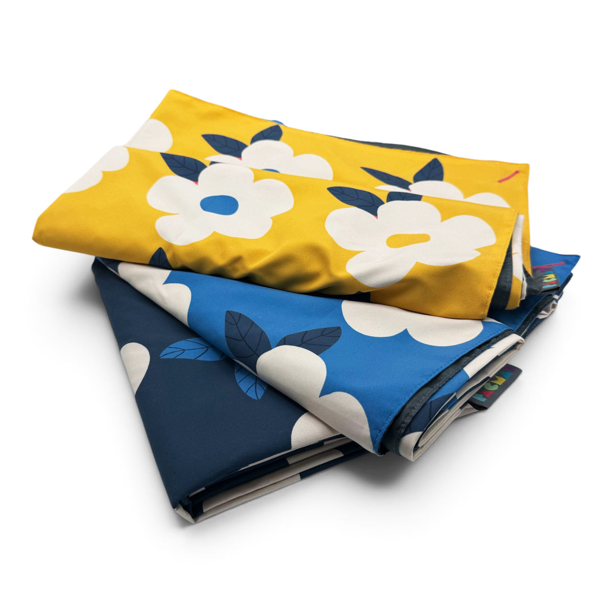 Two folded fabric items with a floral cloud pattern, stacked on a white background. The top item is mustard yellow with large white flowers and dark blue leaves, and the bottom item is blue with the same white and dark blue pattern.