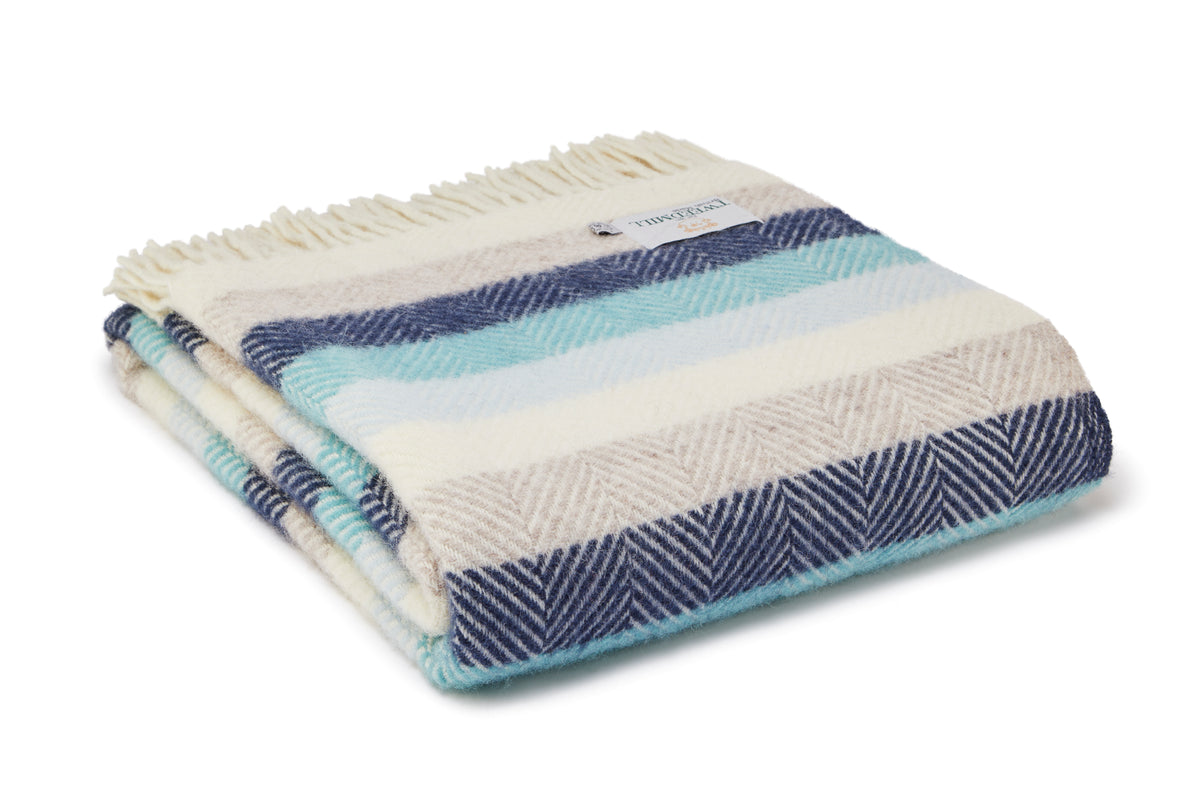A folded woven throw blanket with cream, navy, and light blue stripes, featuring a herringbone pattern and cream fringe on a white background.